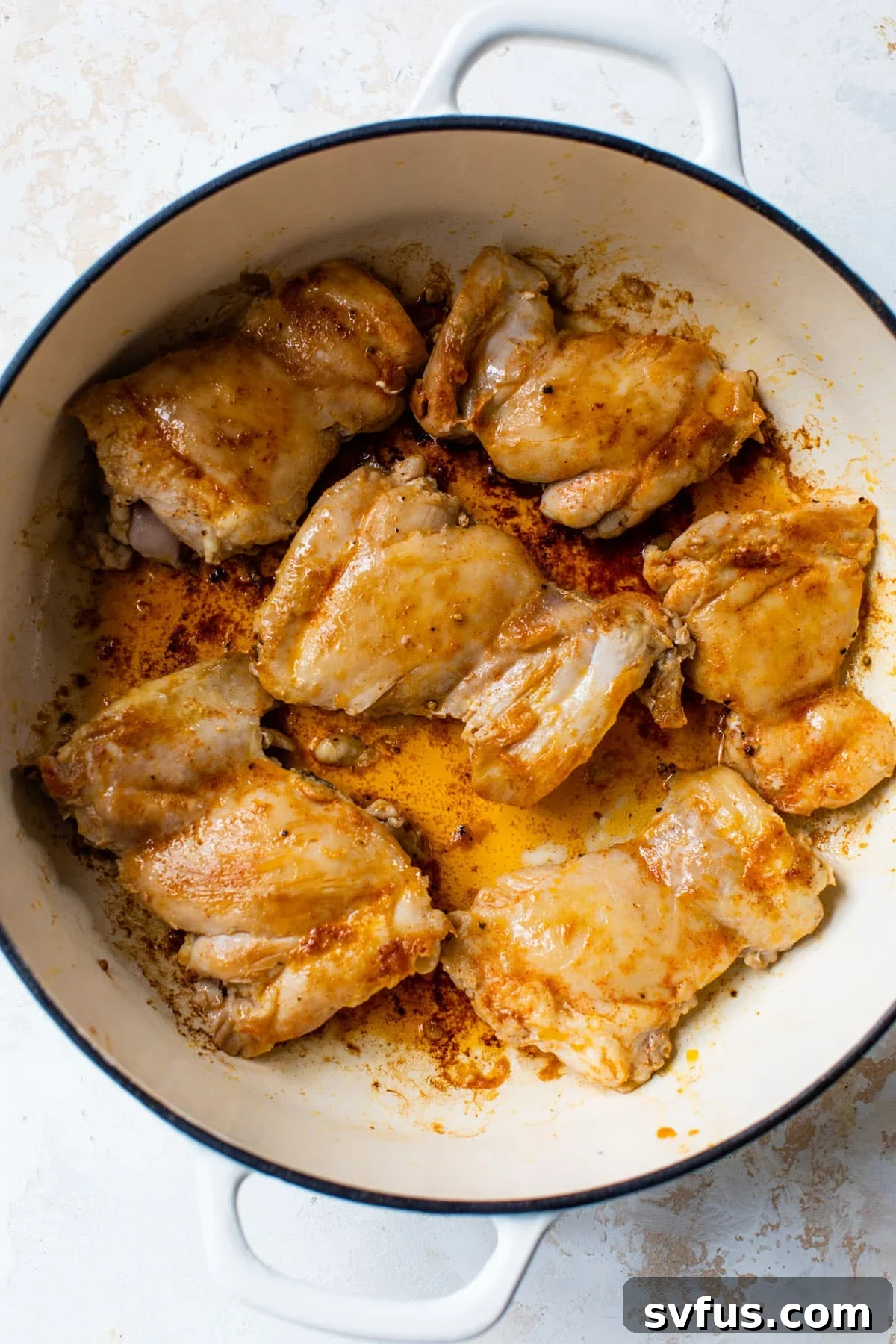 Two boneless, skinless chicken thighs seared to a golden brown perfection in a large skillet, ready to be removed.