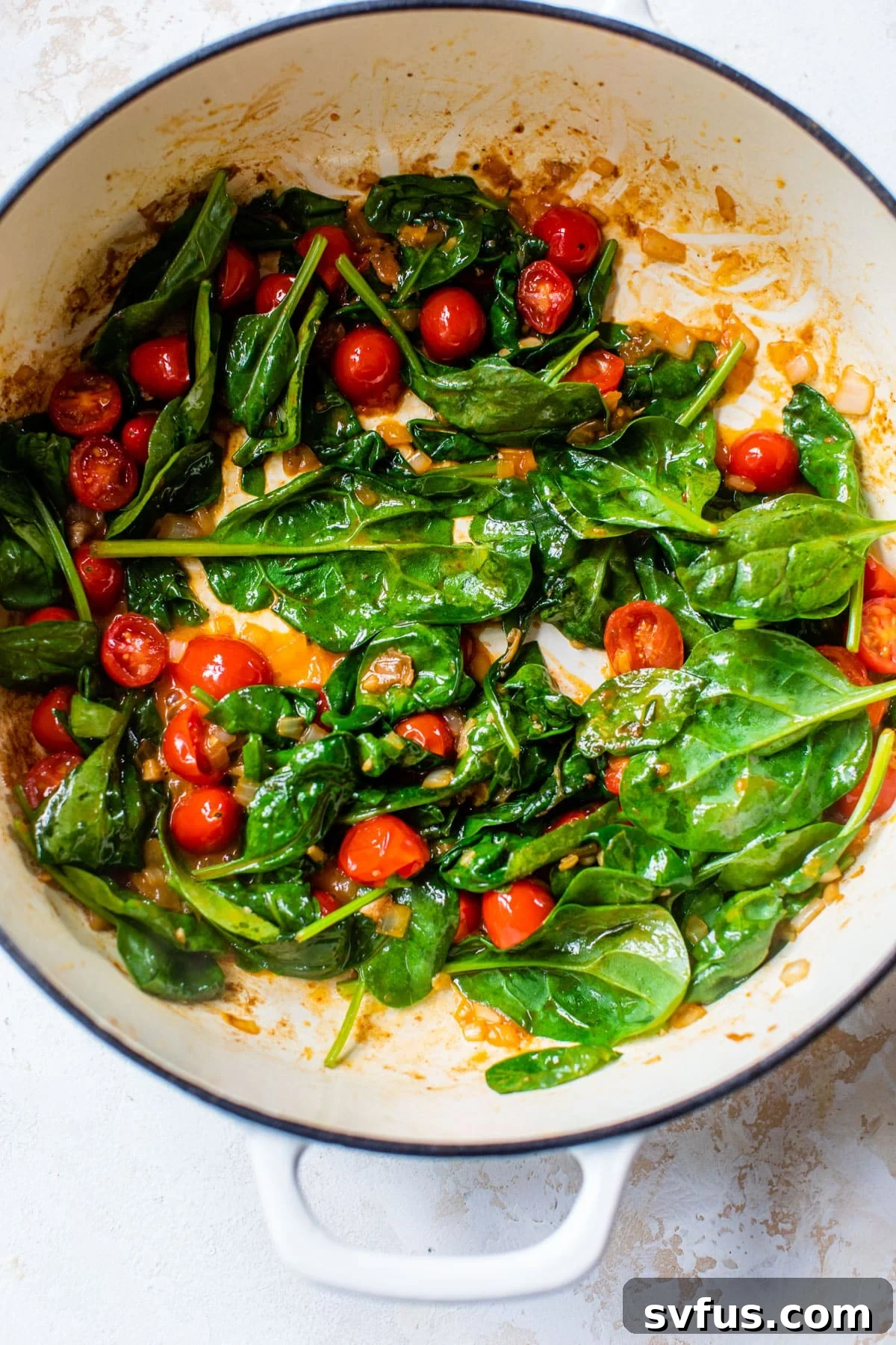 A large skillet containing wilted spinach and softened grape tomatoes, cooked down and ready for the sauce.