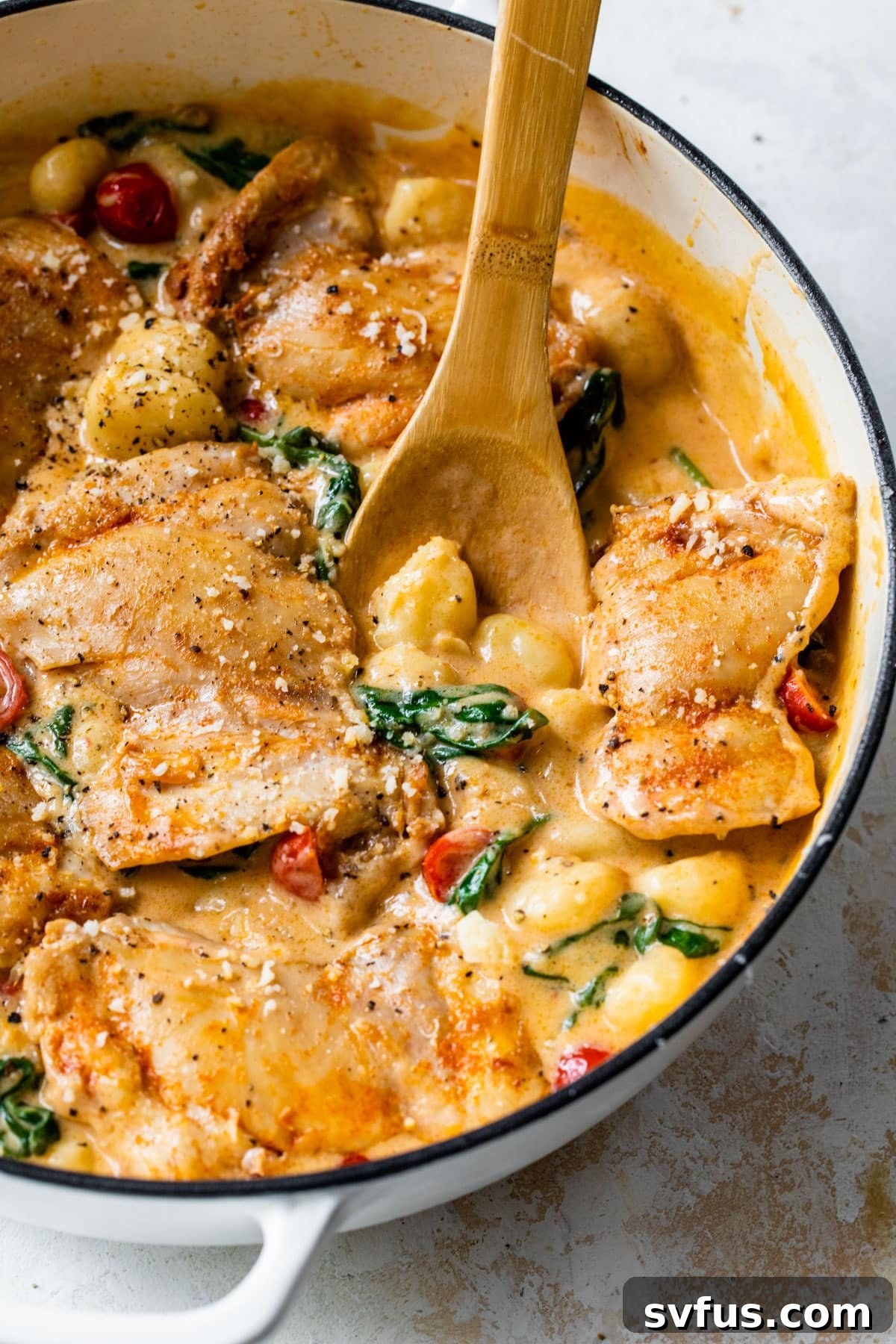 A final shot of the cooked Chicken Gnocchi Skillet in a pan, showcasing golden chicken, creamy gnocchi, vibrant tomatoes, and spinach, garnished and ready to serve.