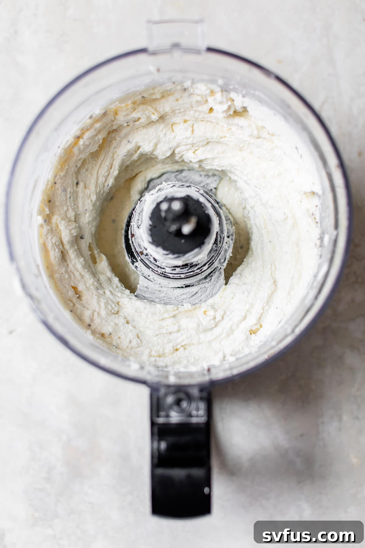 A food processor actively blending feta and cream cheese into a smooth, creamy dip, showcasing the preparation process.