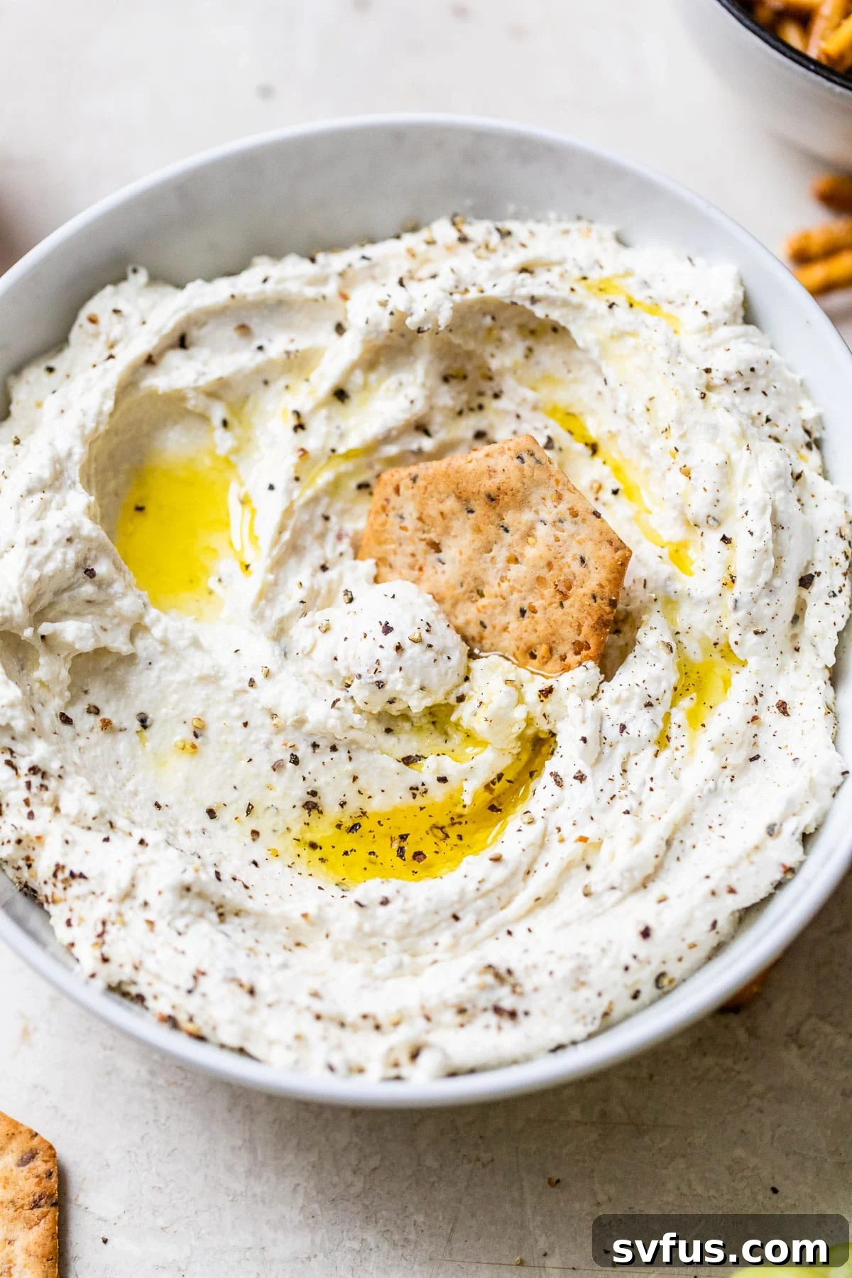 A close-up shot of creamy whipped cheese in a white bowl, with a cracker being dipped into it, highlighting its inviting texture.