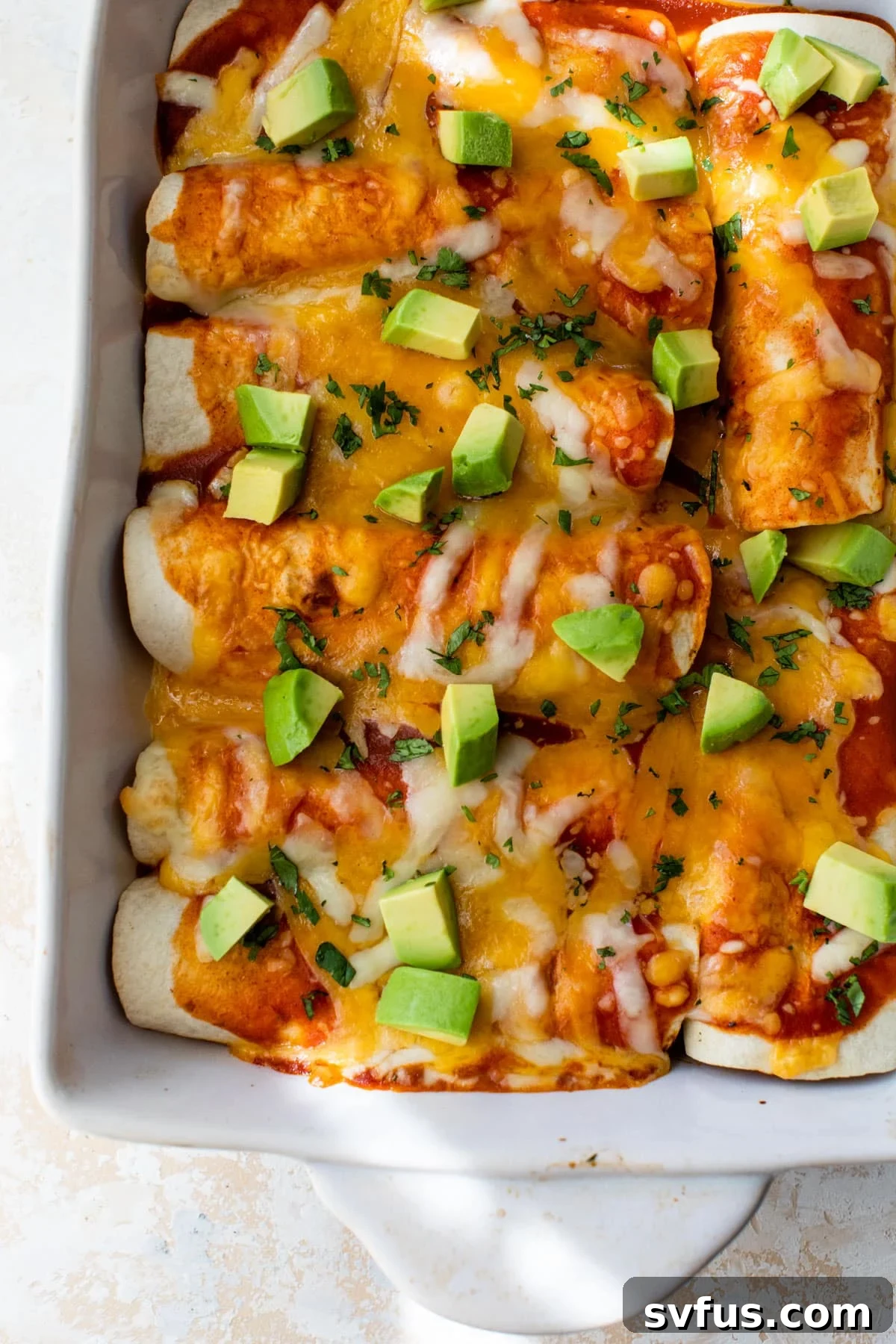 butternut squash enchiladas in a baking dish topped with diced avocado