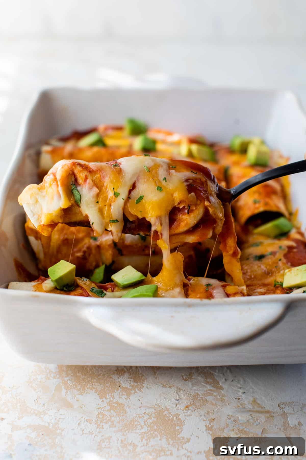 side view of a butternut squash enchilada being removed from a baking dish topped with diced avocado