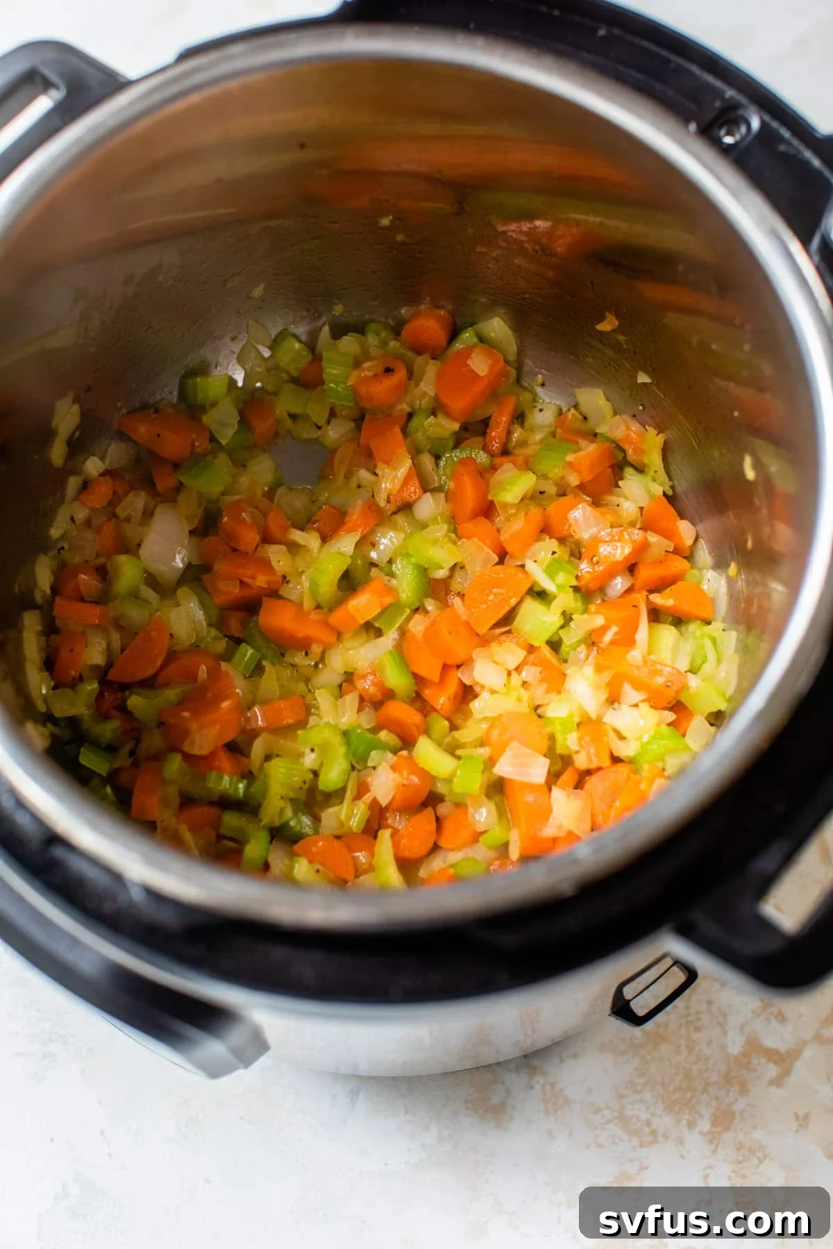 Chopped onion, carrots, and celery cooking down in the Instant Pot with butter, creating a fragrant mirepoix base for the soup.