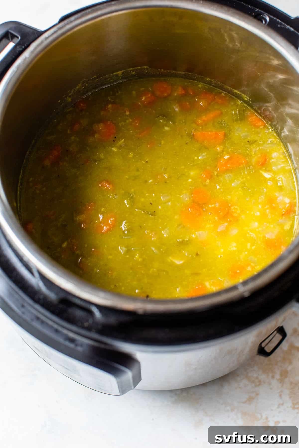 Bay leaves, salt, pepper, split peas, and broth added to the Instant Pot with sautéed vegetables, ready for pressure cooking.