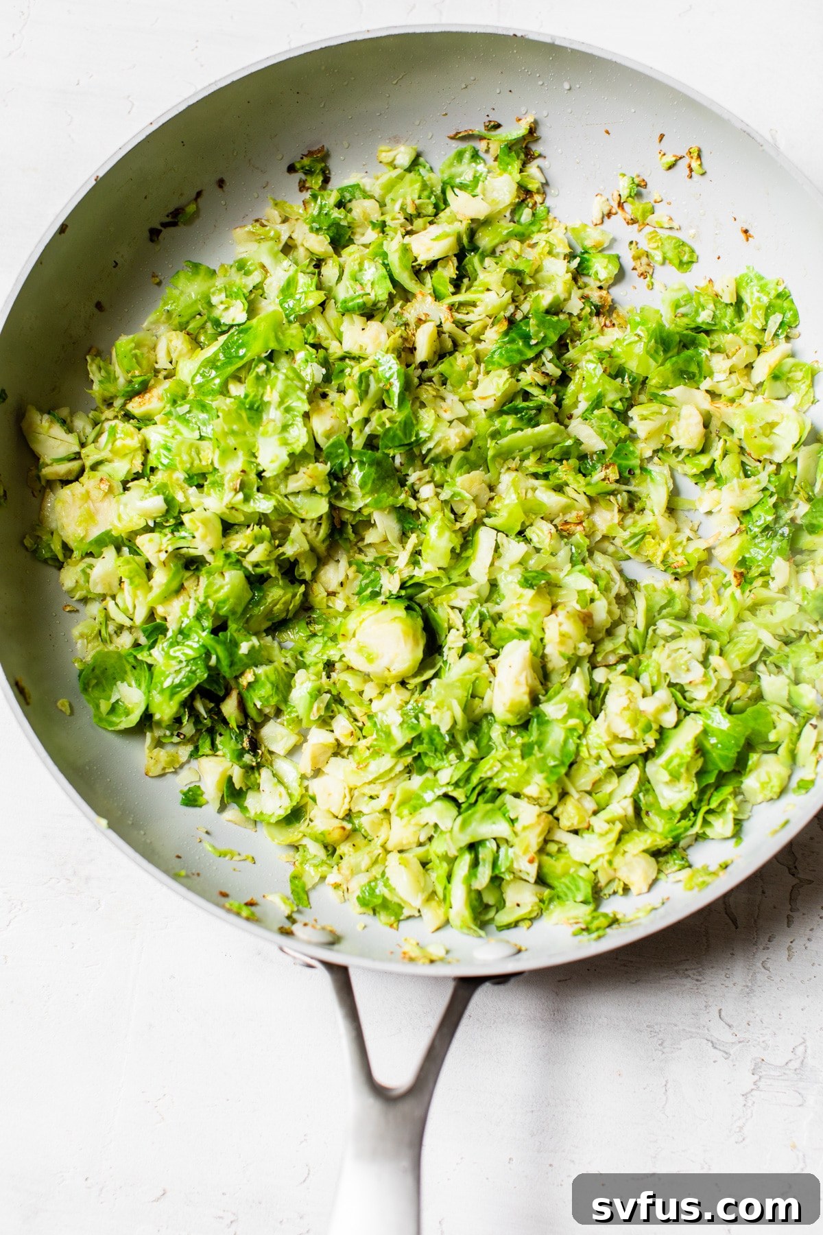 Shredded Brussels sprouts sautéing in a skillet, developing a golden-brown color