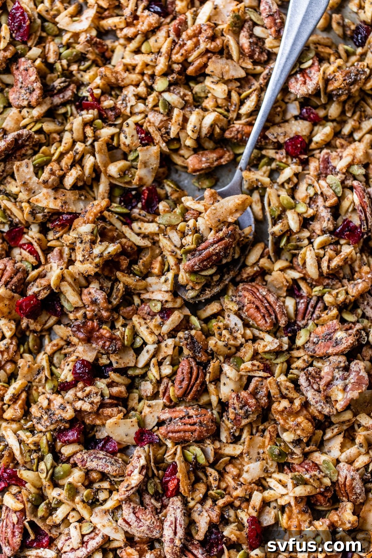granola on a baking sheet with a spoon, highlighting its golden crunch