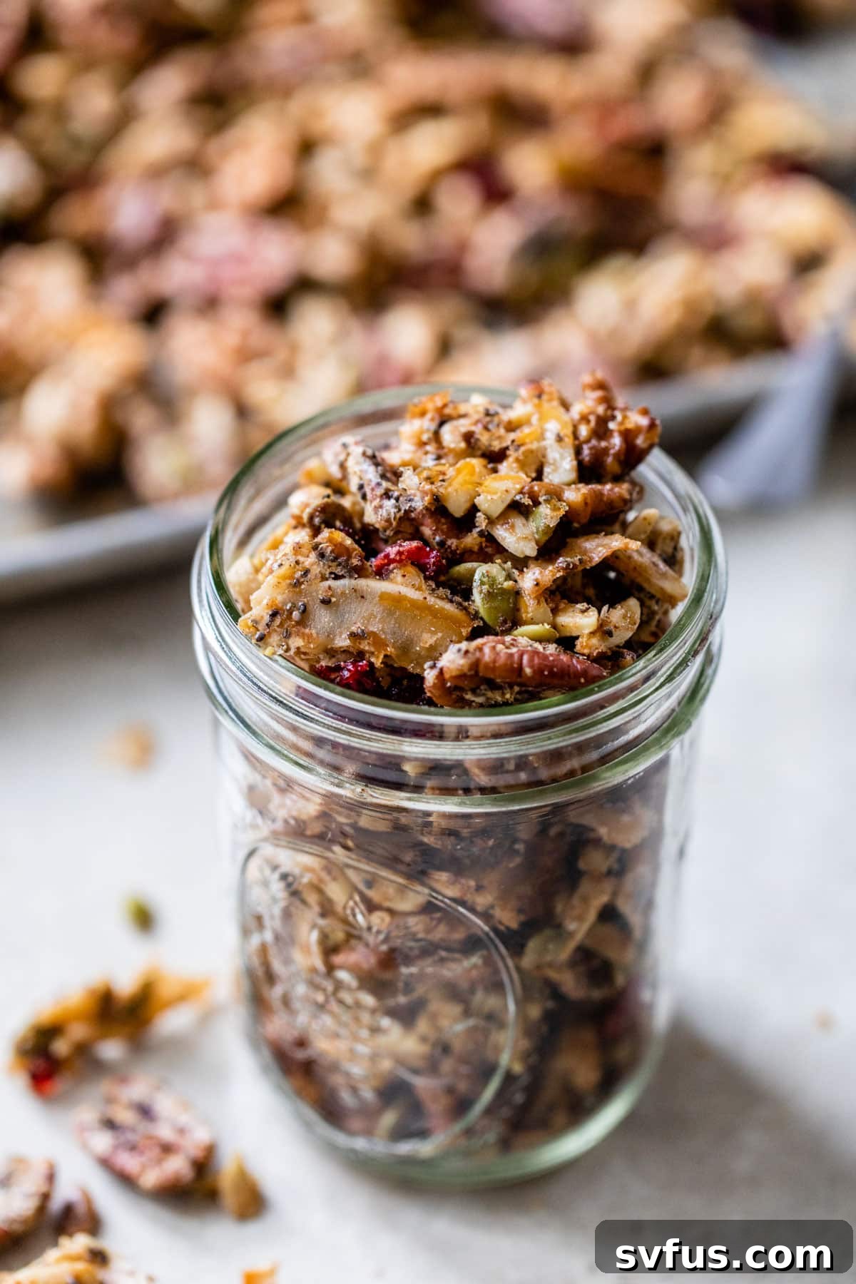 glass jar with granola in front of a baking sheet with granola, showcasing the finished product