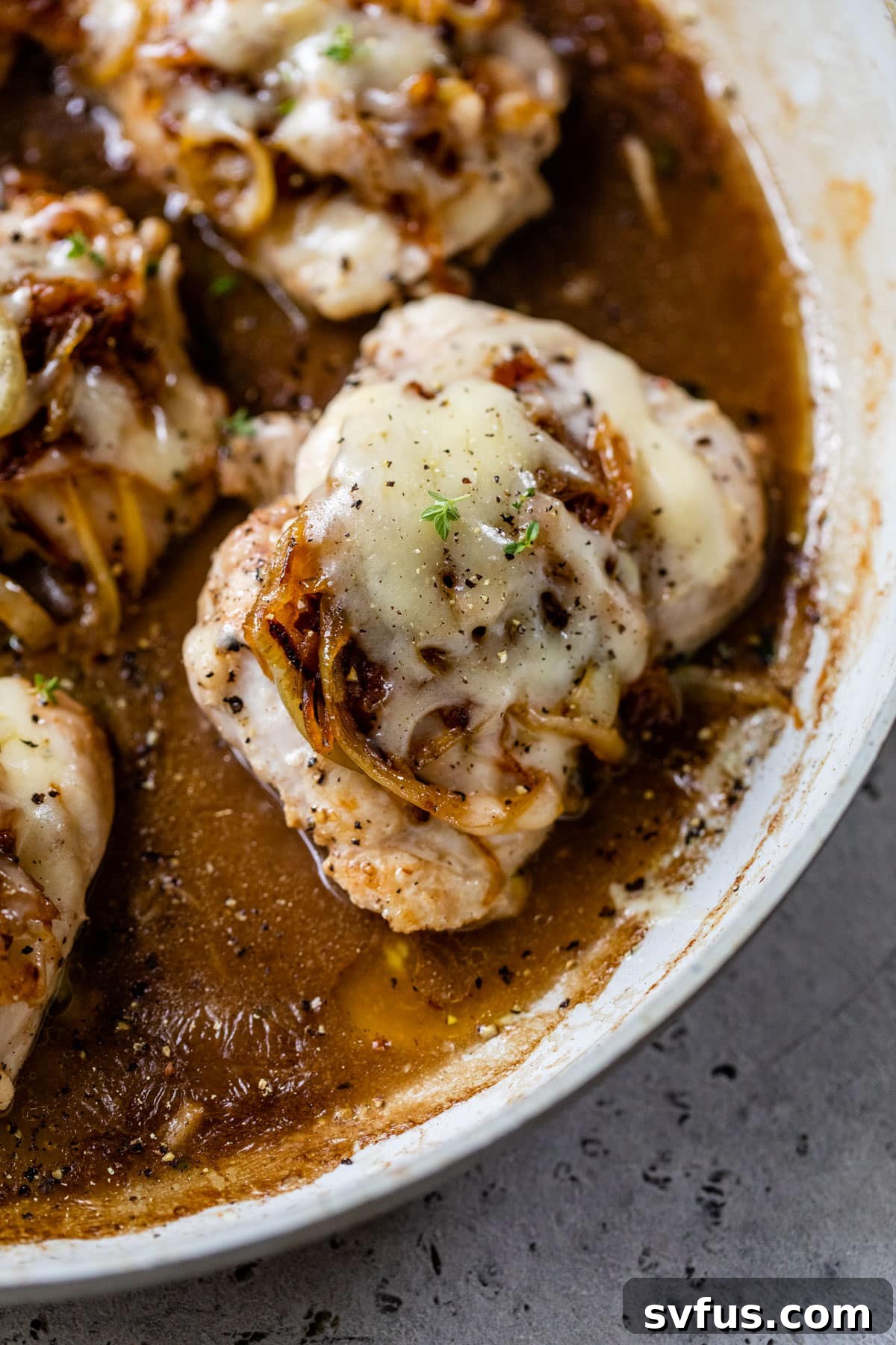 close up of a cooked boneless chicken thighs in a skillet topped with caramelized onions and melty cheese