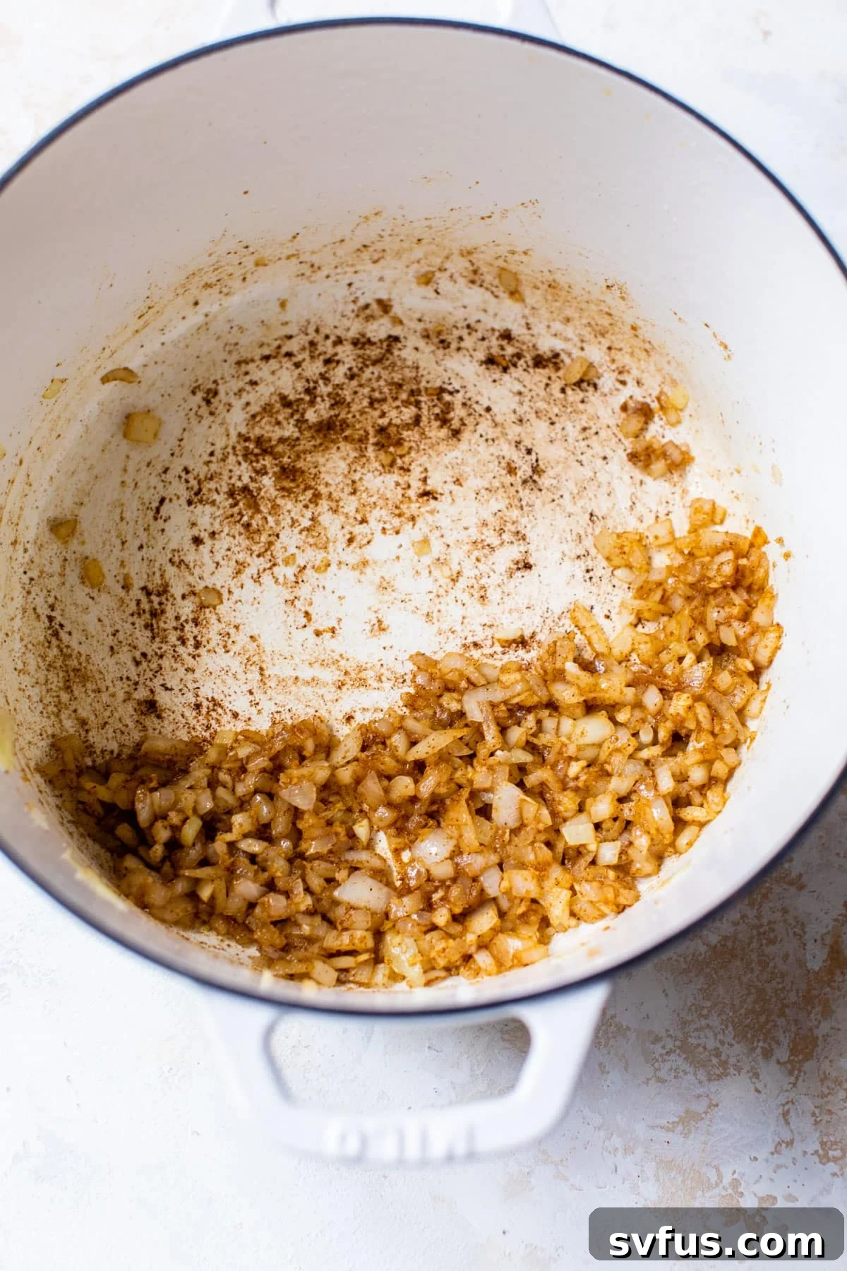 A large pot showing cooked diced onion, fragrant garlic, and vibrant spices melding together, forming the flavorful base of the soup.