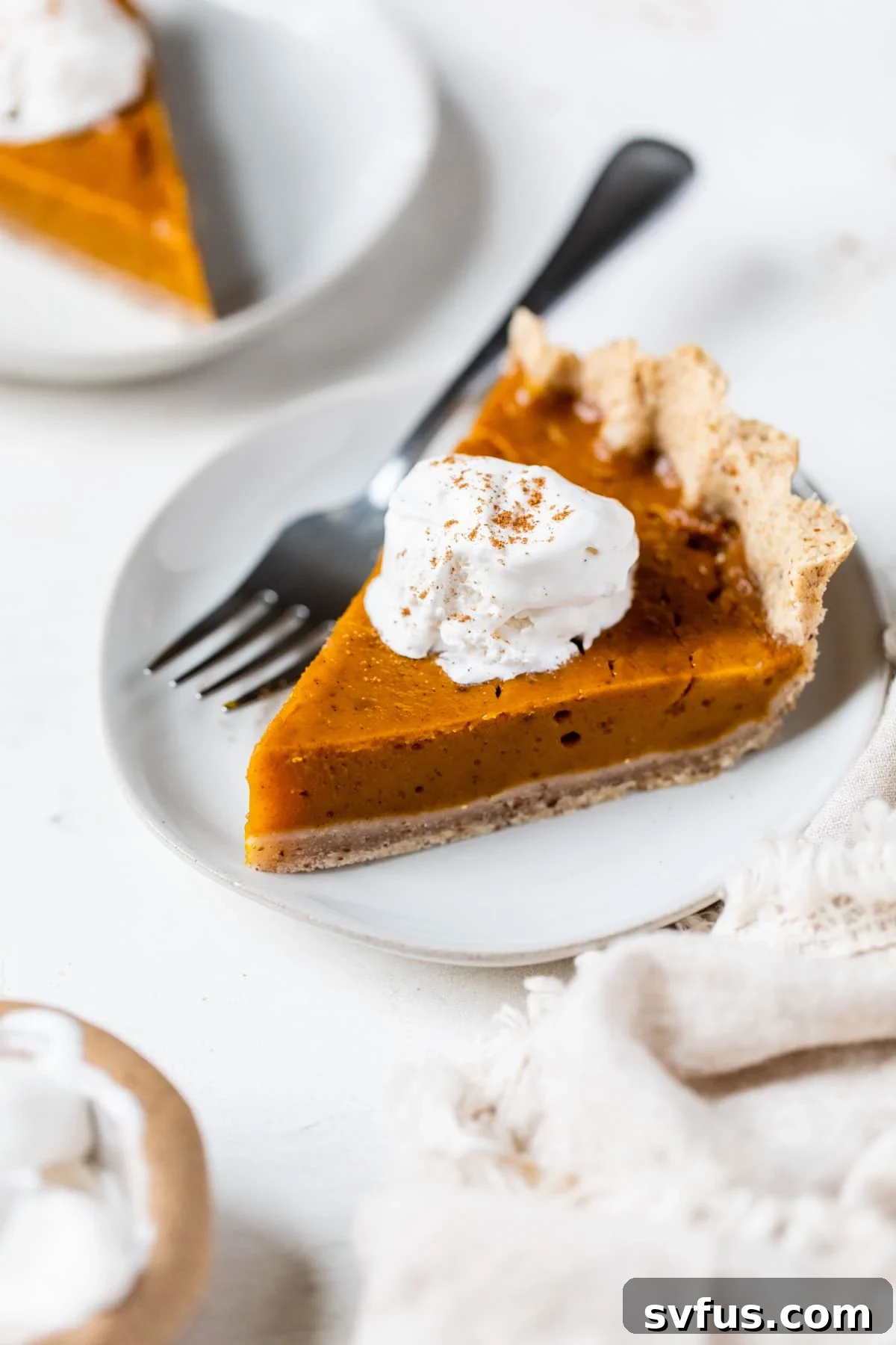 A beautifully sliced vegan pumpkin pie, topped with fluffy vegan whipped cream, served on a white plate ready to be enjoyed.