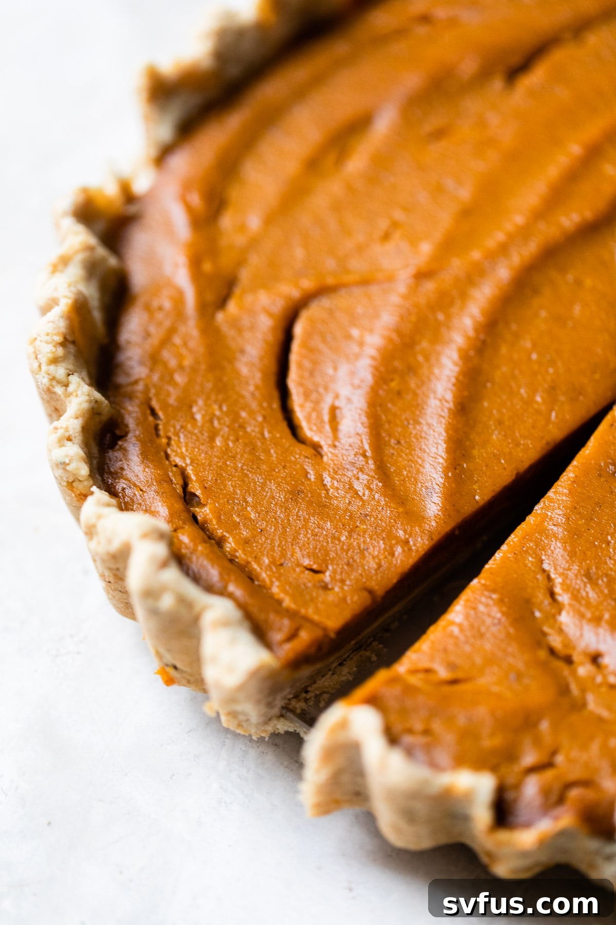 A close-up shot of a baked vegan pumpkin pie, showcasing its smooth, golden-brown surface and crimped crust edges, ready for slicing.