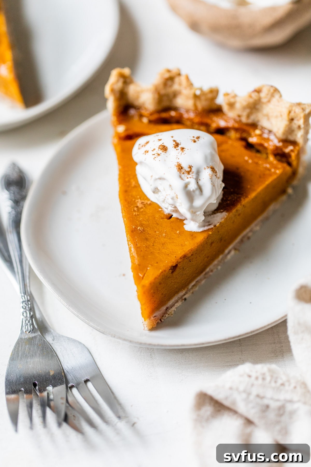 A single slice of vegan pumpkin pie elegantly plated, generously topped with a dollop of vegan whipped cream and a sprinkle of cinnamon.