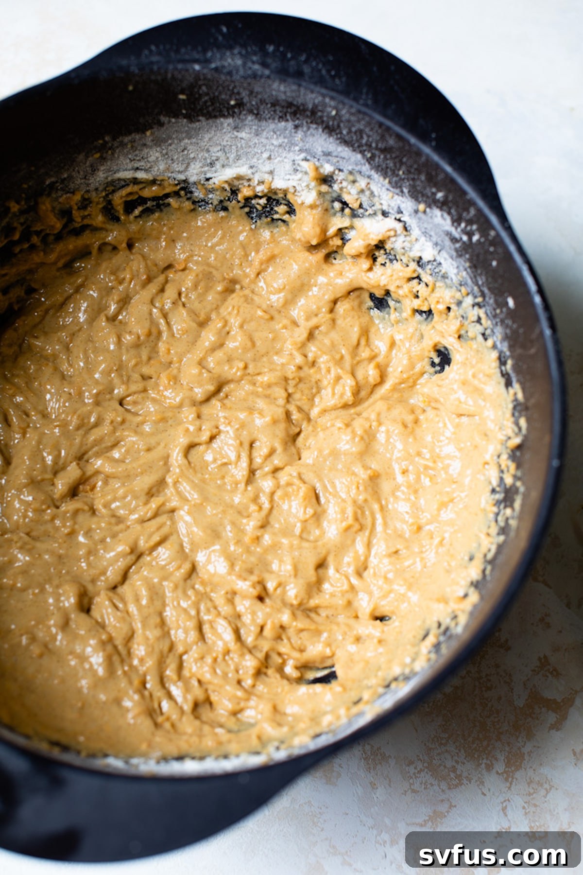 A bowl of creamy, orange-hued sweet potato muffin batter, ready to be spooned into muffin liners, showcasing its smooth texture.