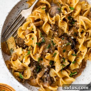 mushroom stroganoff inside a bowl with a fork and fresh parsley and cheese on top
