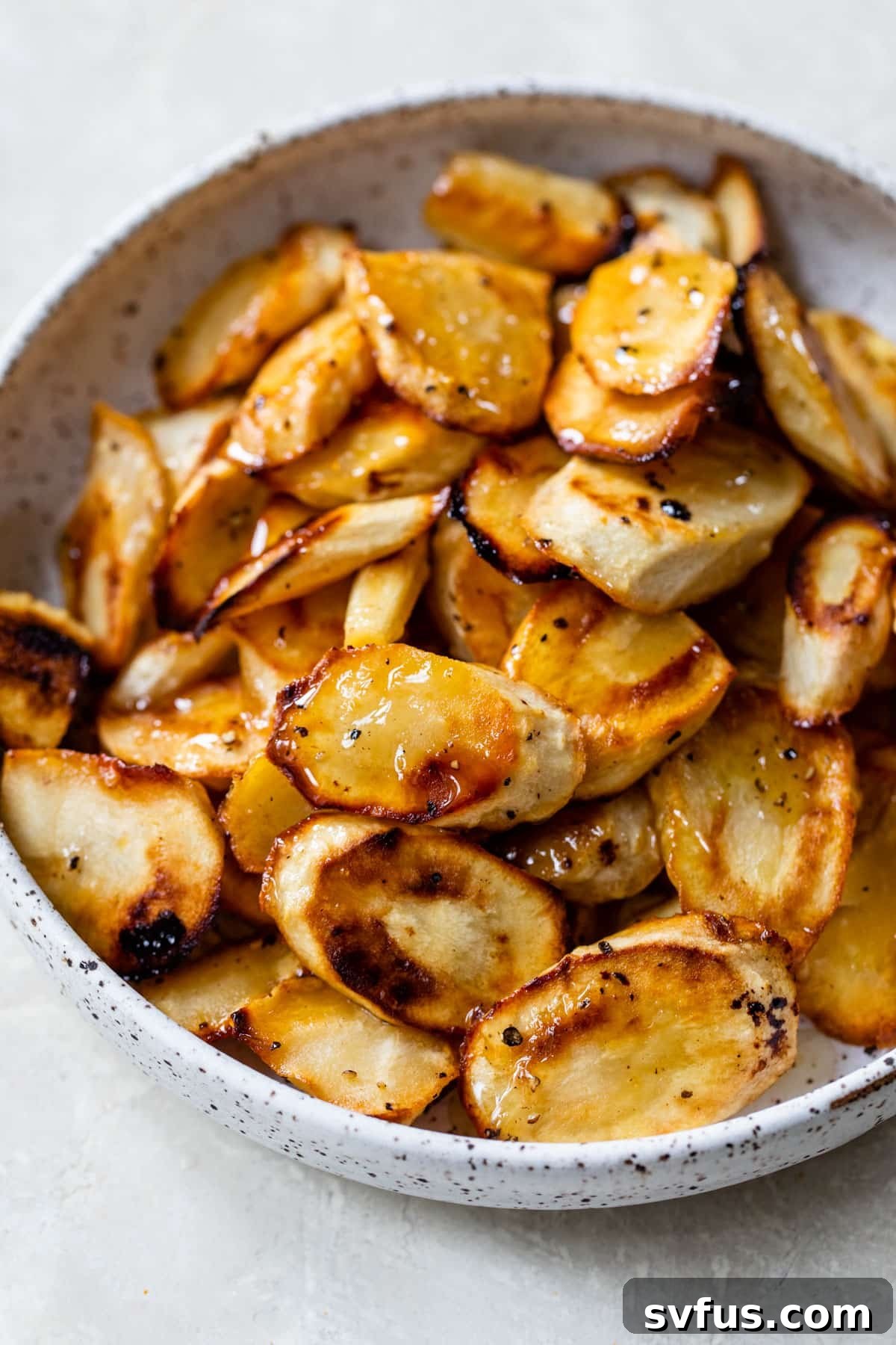 A bowl filled with golden-brown honey roasted parsnips, garnished with fresh herbs, ready to be served as a healthy and flavorful side dish.