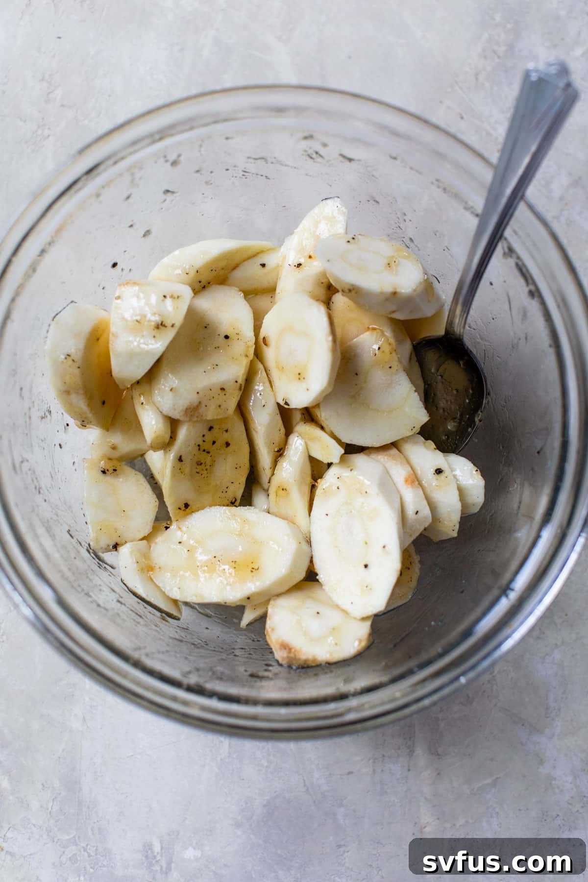 Raw parsnip slices in a glass bowl, partially coated with honey glaze, ready for roasting.