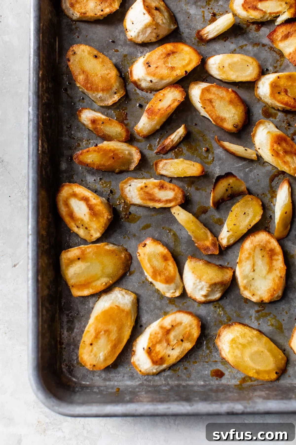 Honey glazed parsnips spread evenly on a baking sheet lined with parchment paper, ready for the oven.