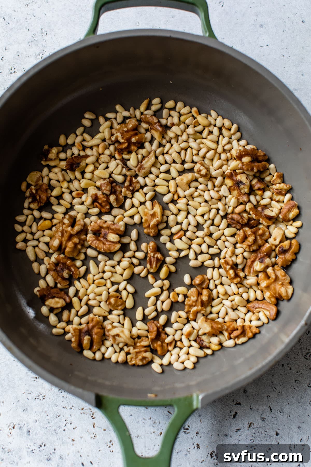 Pine nuts and walnuts gently toasting in a dry skillet, releasing their nutty aroma.