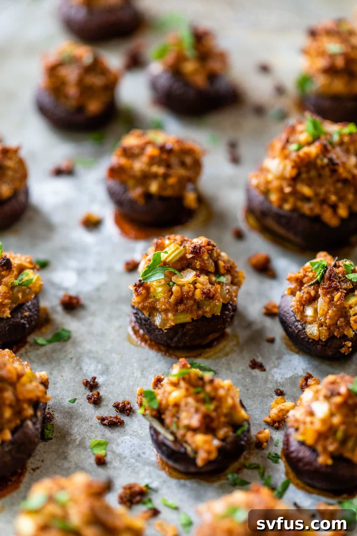A baking sheet filled with perfectly golden-brown vegan stuffed mushrooms, fresh out of the oven and ready to be garnished.
