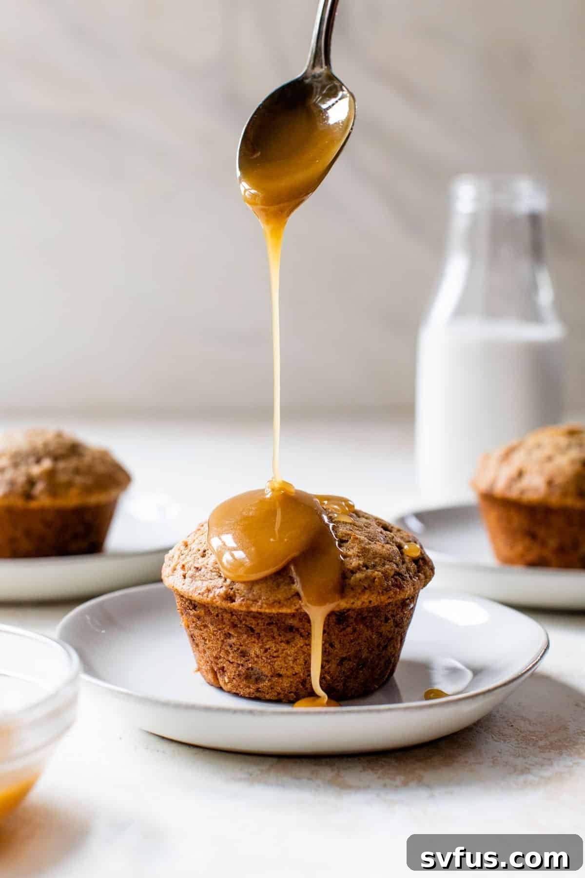 A stunning vegan sticky toffee pudding on a plate, generously drizzled with golden caramel sauce and accompanied by a spoon, ready to be enjoyed.