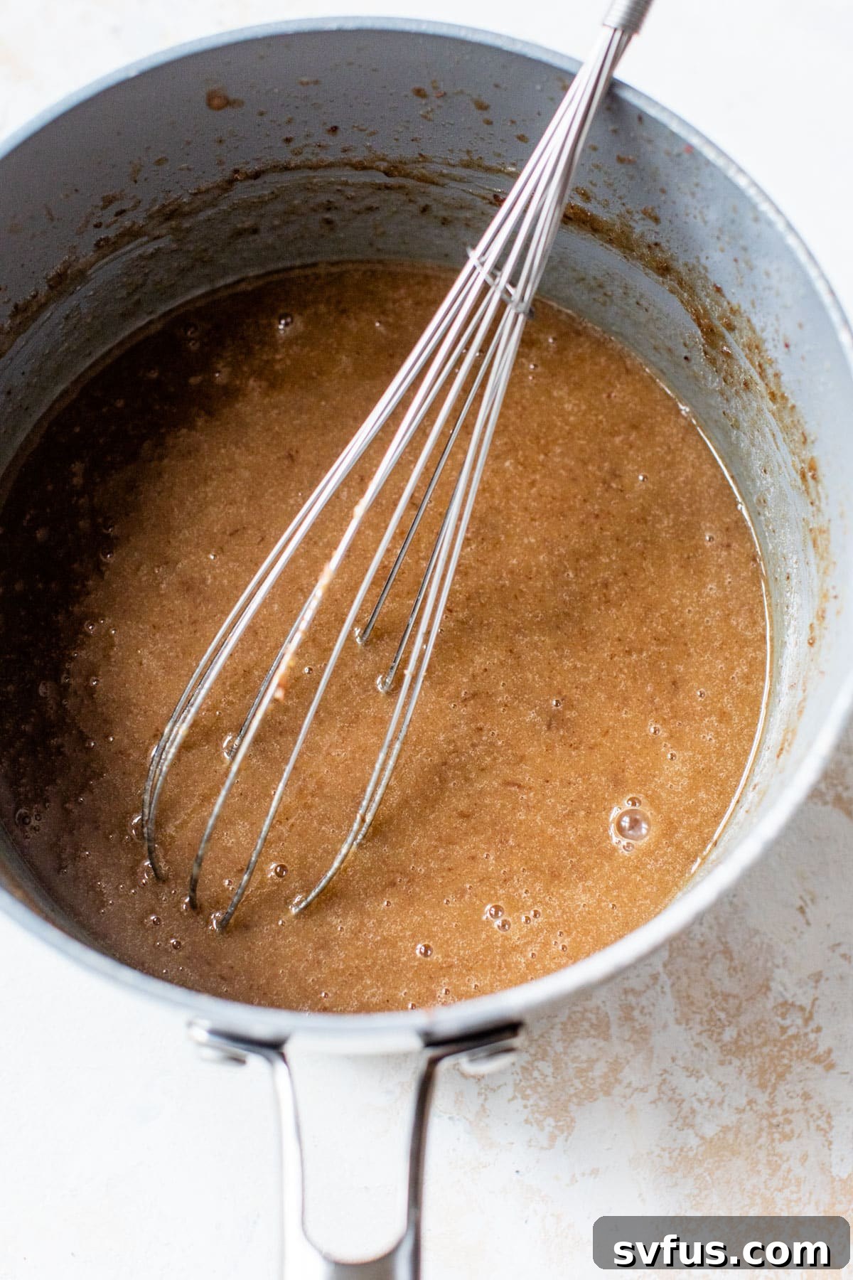 The date mixture, now combined with melted vegan butter and brown sugar, being whisked in a saucepan to create a smooth and rich wet base for the pudding.