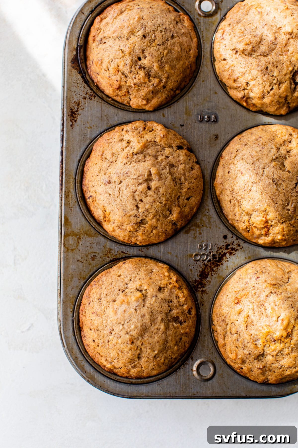 Freshly baked vegan sticky toffee puddings resting in a large muffin tin, golden brown and perfectly risen, cooling before the sauce is added.