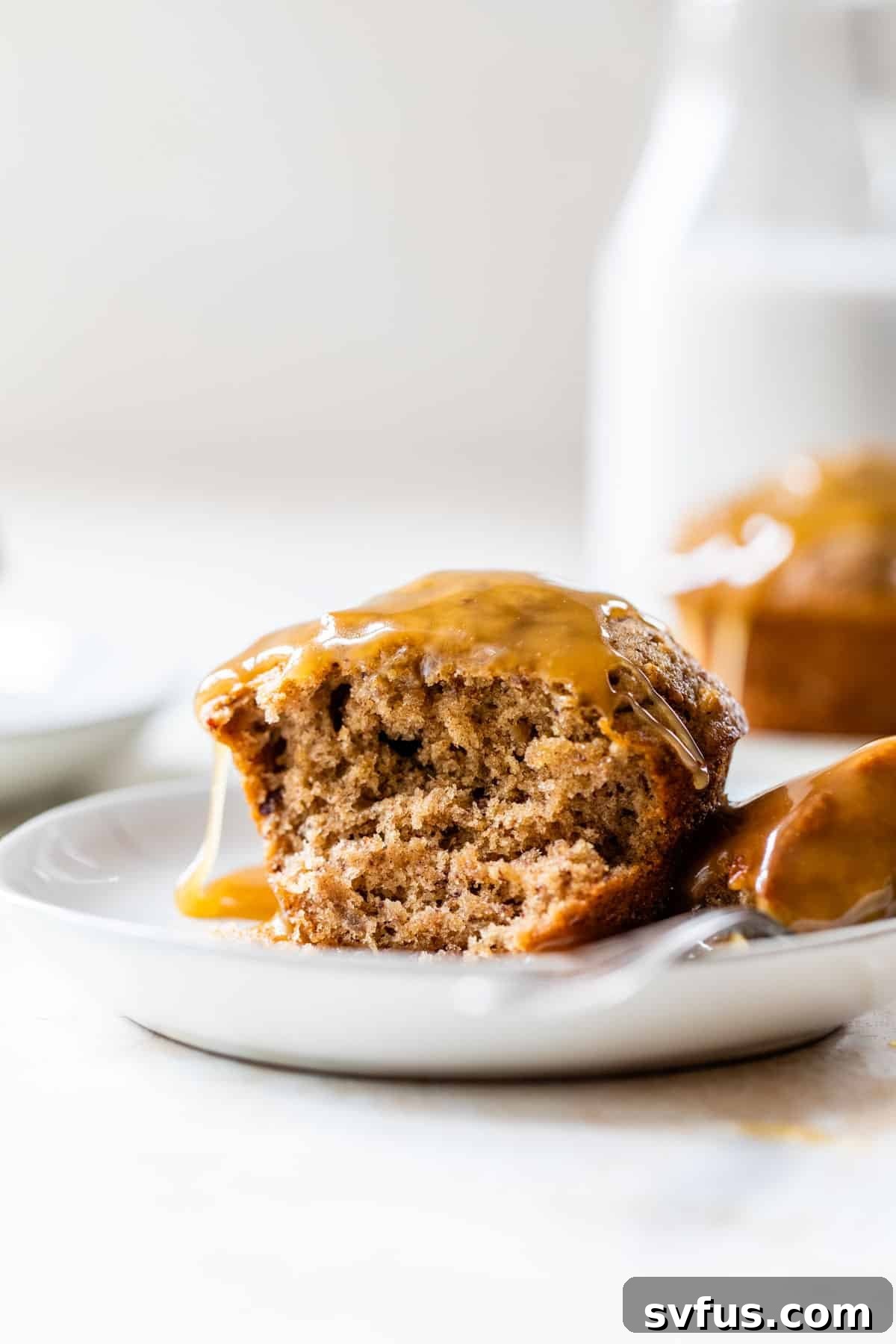 A second close-up view of the delicious vegan sticky toffee pudding, artfully plated with a spoon and an abundance of rich caramel sauce on top.