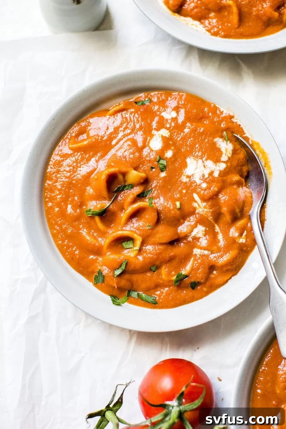 Hearty bowl of vegan tomato soup with gluten-free pasta, garnished with fresh herbs.