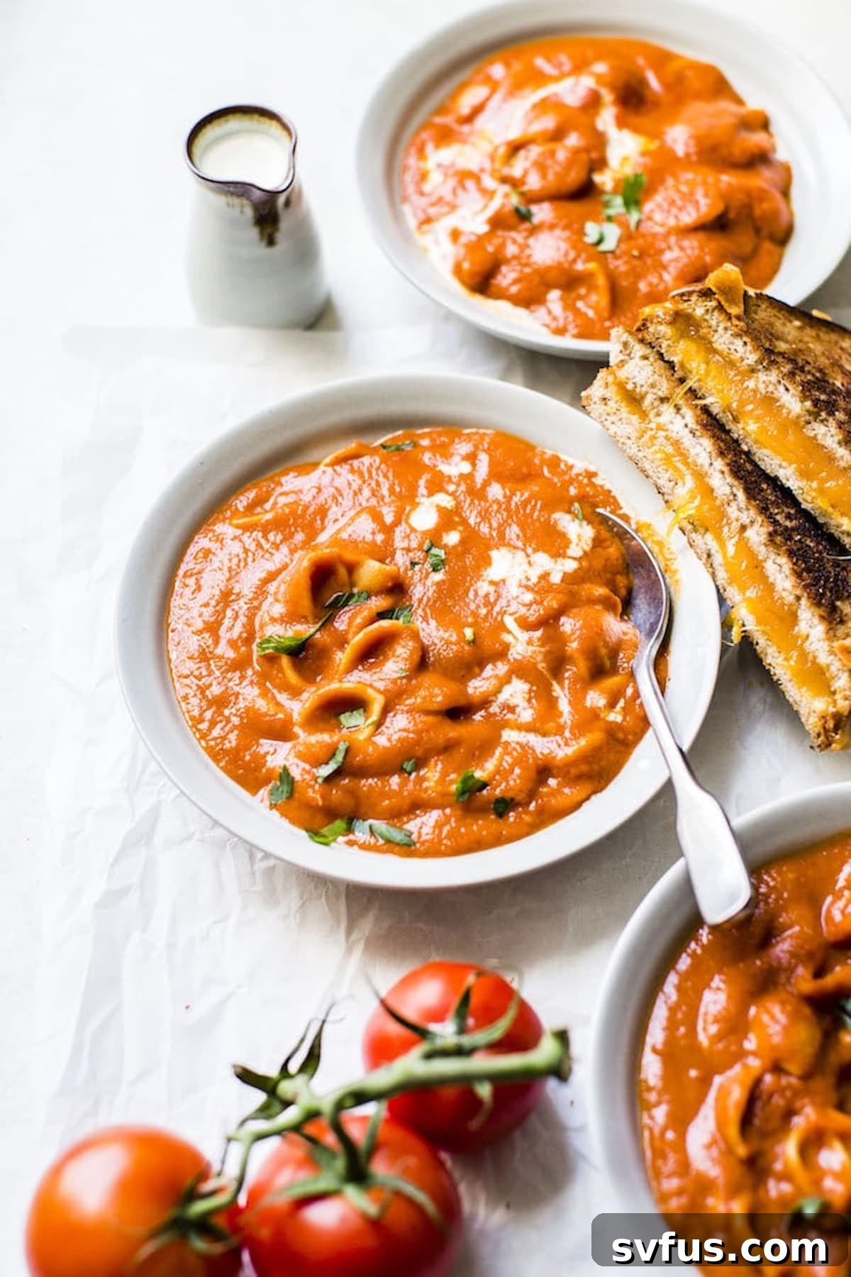 A beautifully presented bowl of vegan tomato soup with pasta, accompanied by a golden grilled cheese sandwich, set on a dark background.