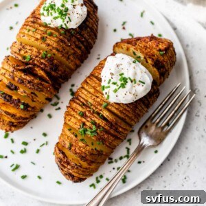 Two hasselback potatoes with sour cream and chives on top on a plate with a fork