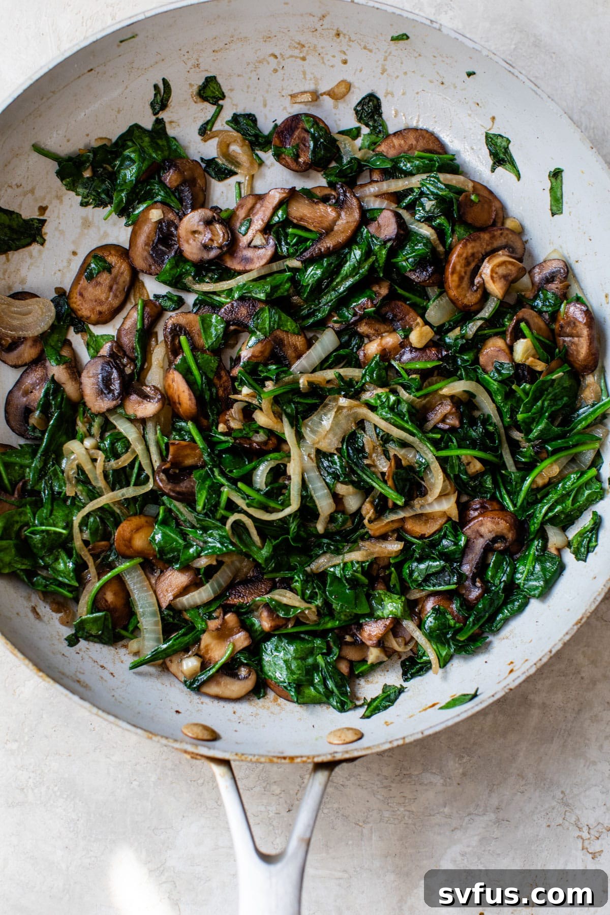 spinach, mushrooms, and onion cooking in a skillet