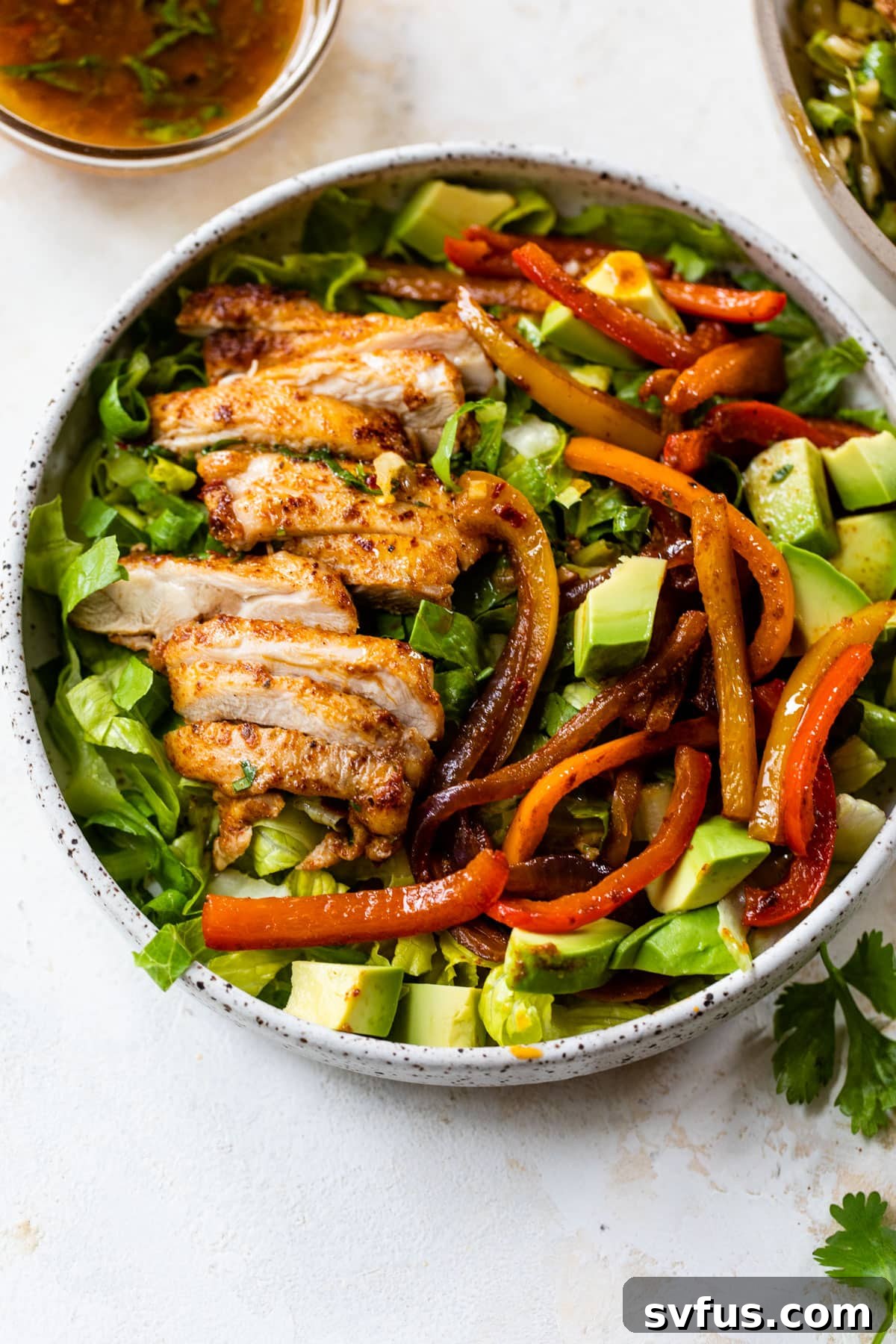 salad in a bowl topped with sliced chicken, bell peppers and diced avocado