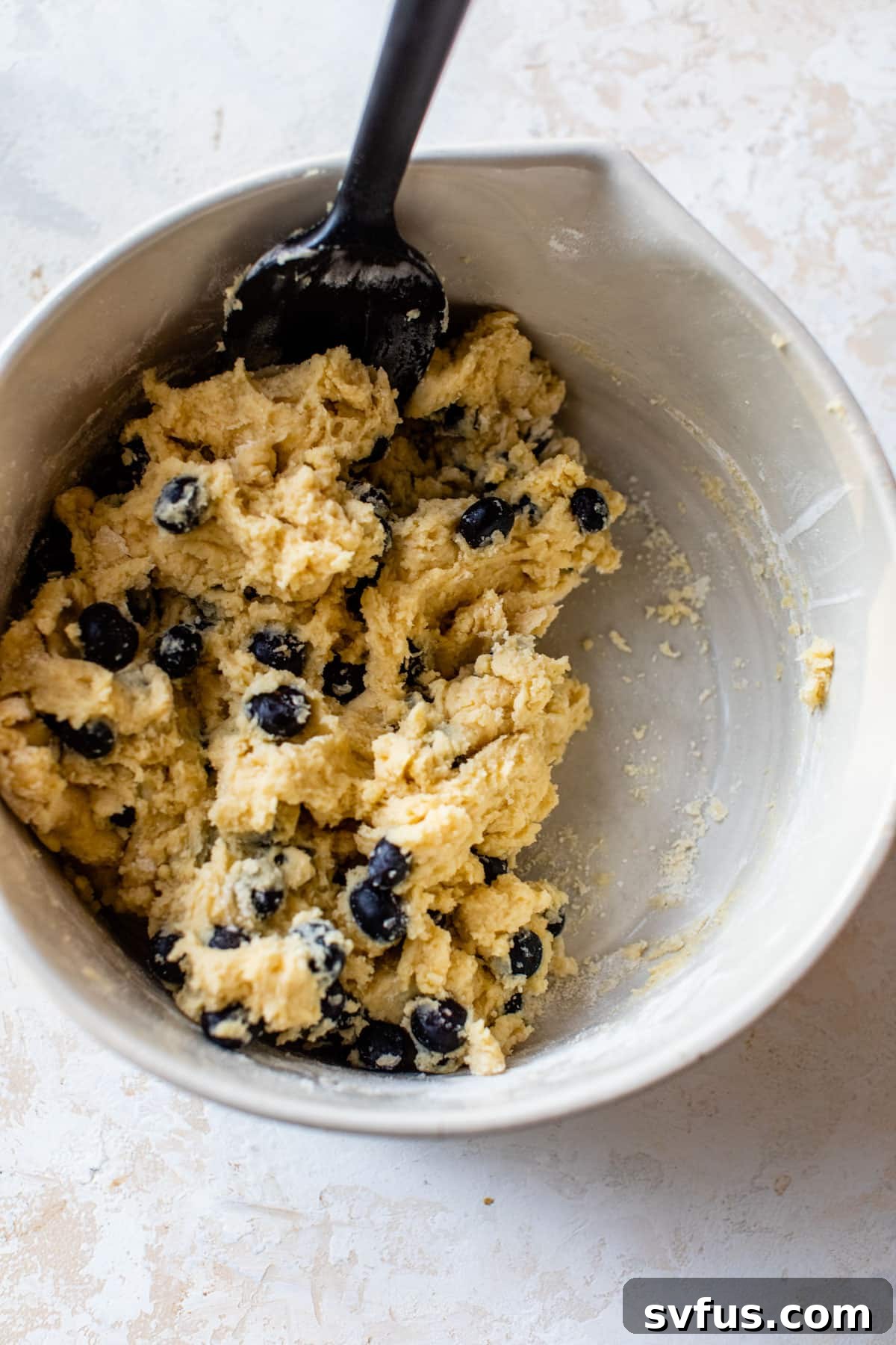 Mixing bowl filled with coffee cake batter and fresh blueberries, ready for baking.