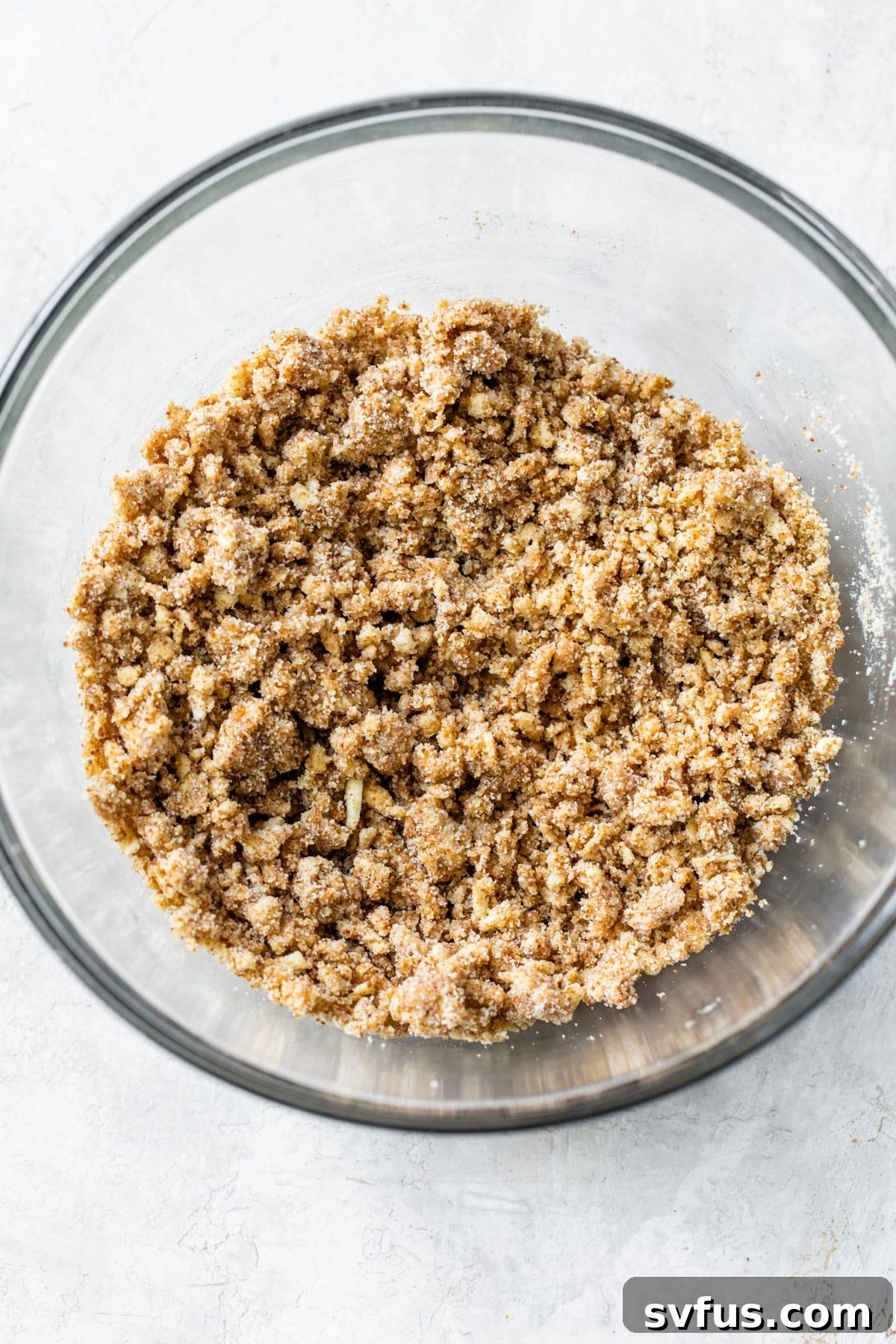 A large glass bowl filled with a crumbly almond flour mixture, showcasing its texture before butter and flax eggs are fully incorporated, ready for the next step of bar preparation.