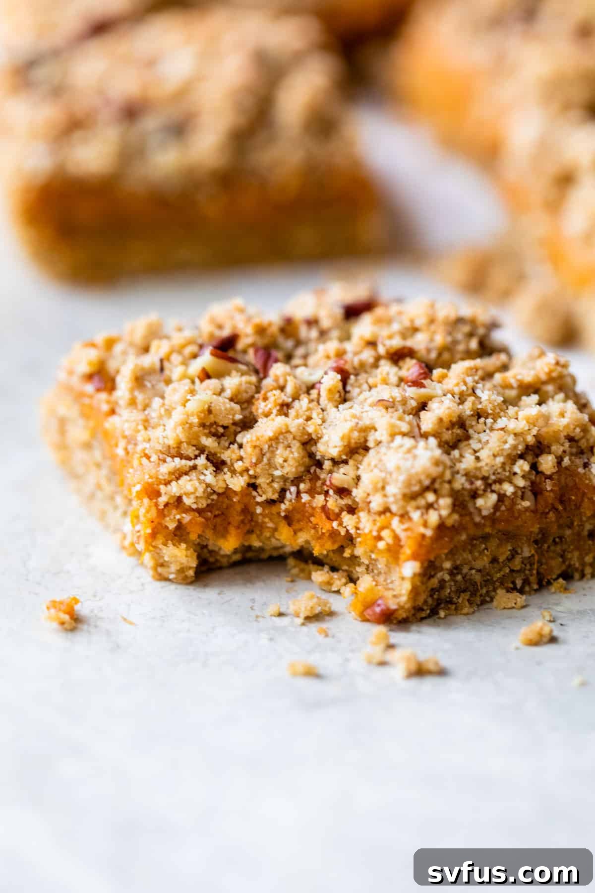 A single sweet potato crumb bar on parchment paper, with a perfect bite taken out, revealing the soft, bright orange filling and the golden, textured crumb topping, inviting a taste.