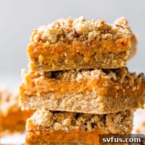 A stack of three golden-brown sweet potato bars with a visible crumb topping, showcasing their delicious layers and readiness to be served.