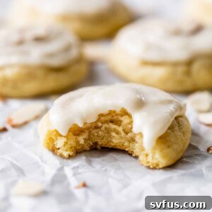 Side view of an almond sugar cookie with a bite taken out, highlighting its soft texture and white frosting.