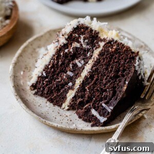 A piece of chocolate cake on a plate with white icing and a fork