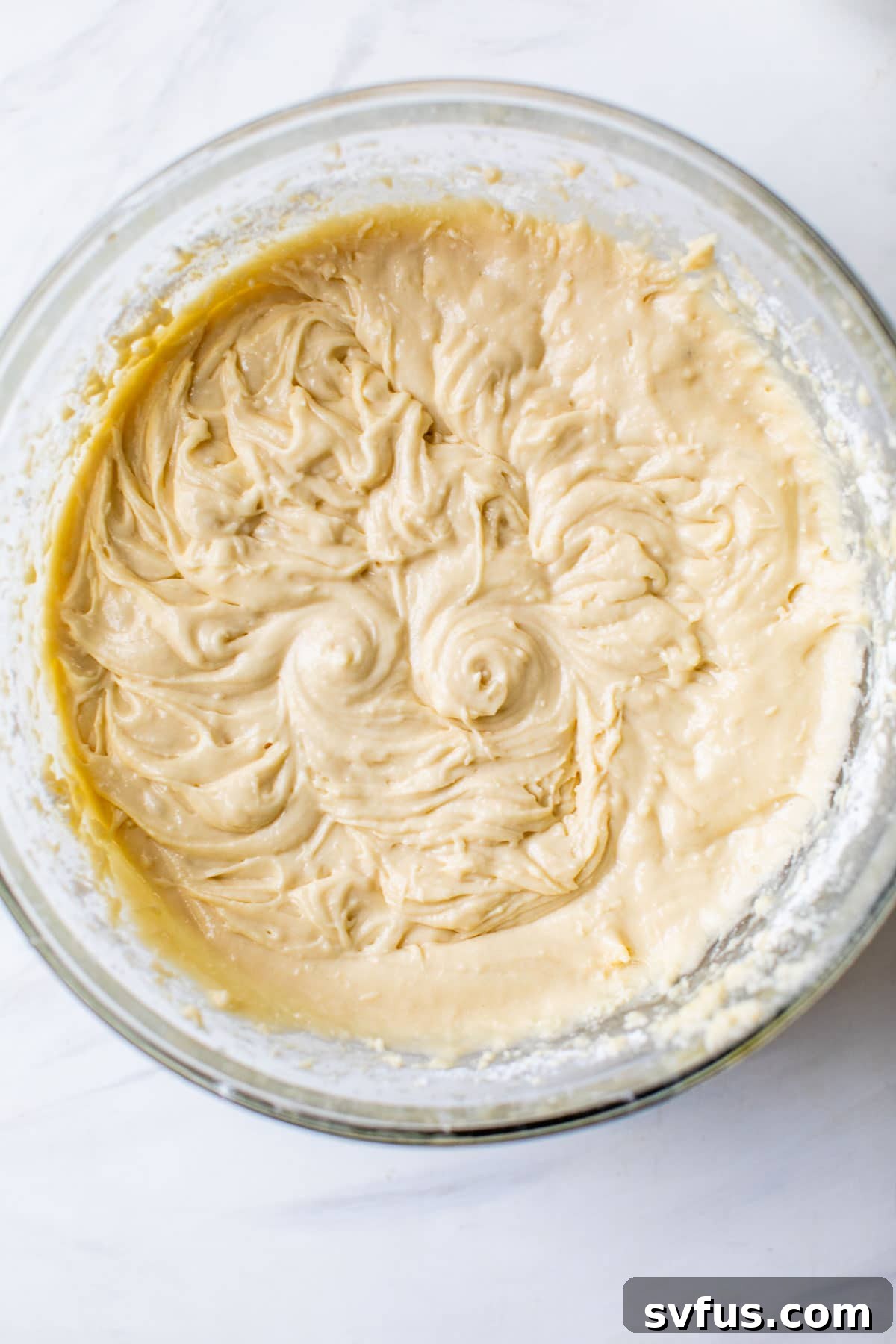 Golden yellow cake batter in a large clear glass bowl, ready for baking.