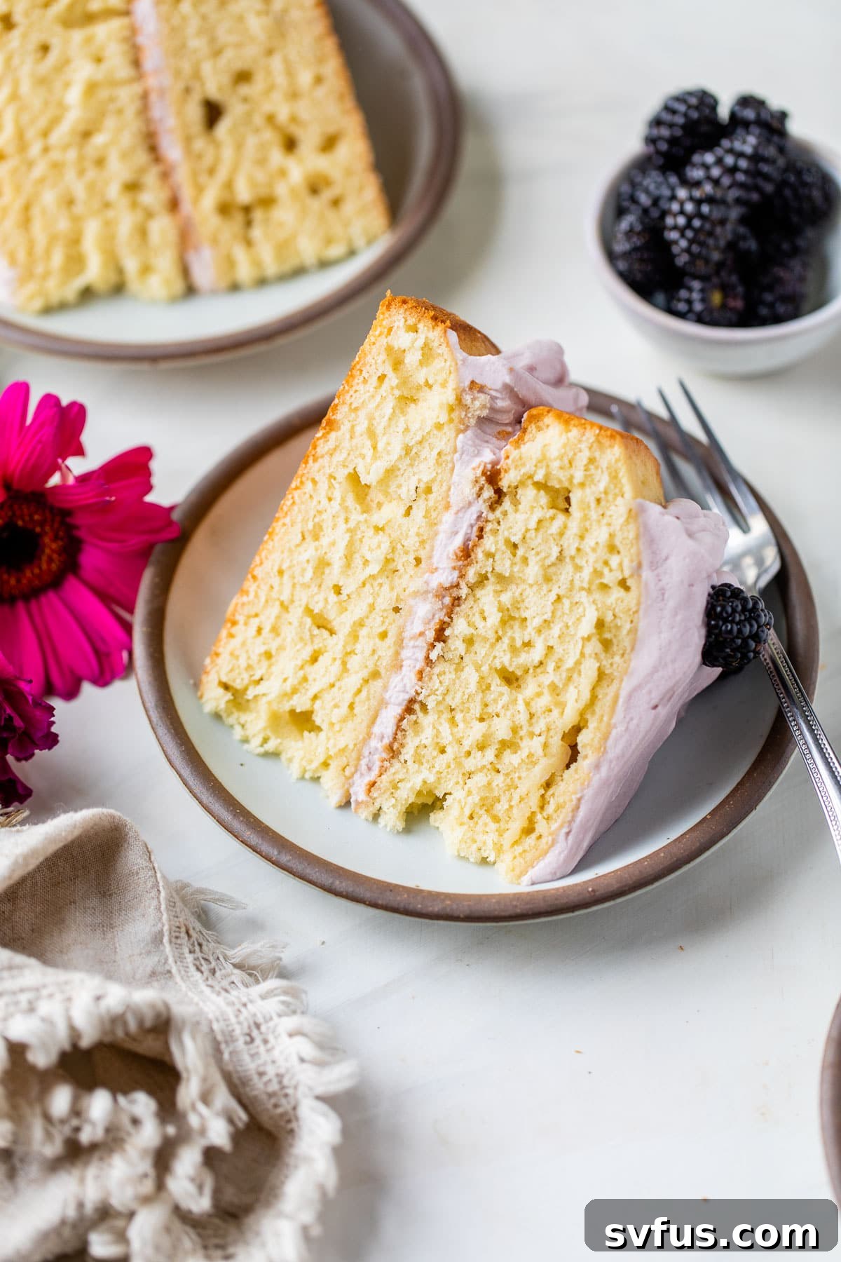 A delightful slice of moist yellow cake on a white plate, generously topped with vibrant purple blackberry lavender icing.