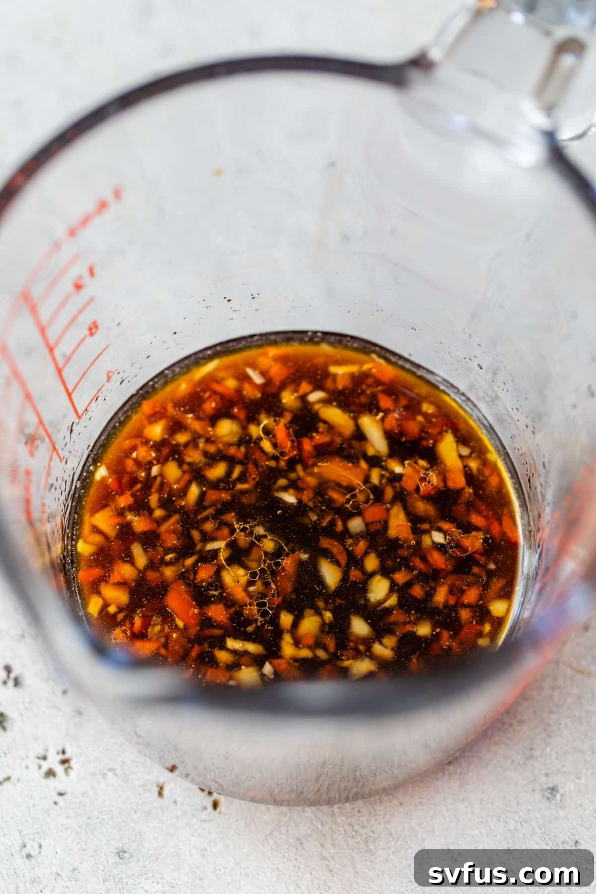 All the ingredients for the homemade Thai steak salad dressing, including soy sauce, lime juice, and chili, mixed in a glass measuring cup.