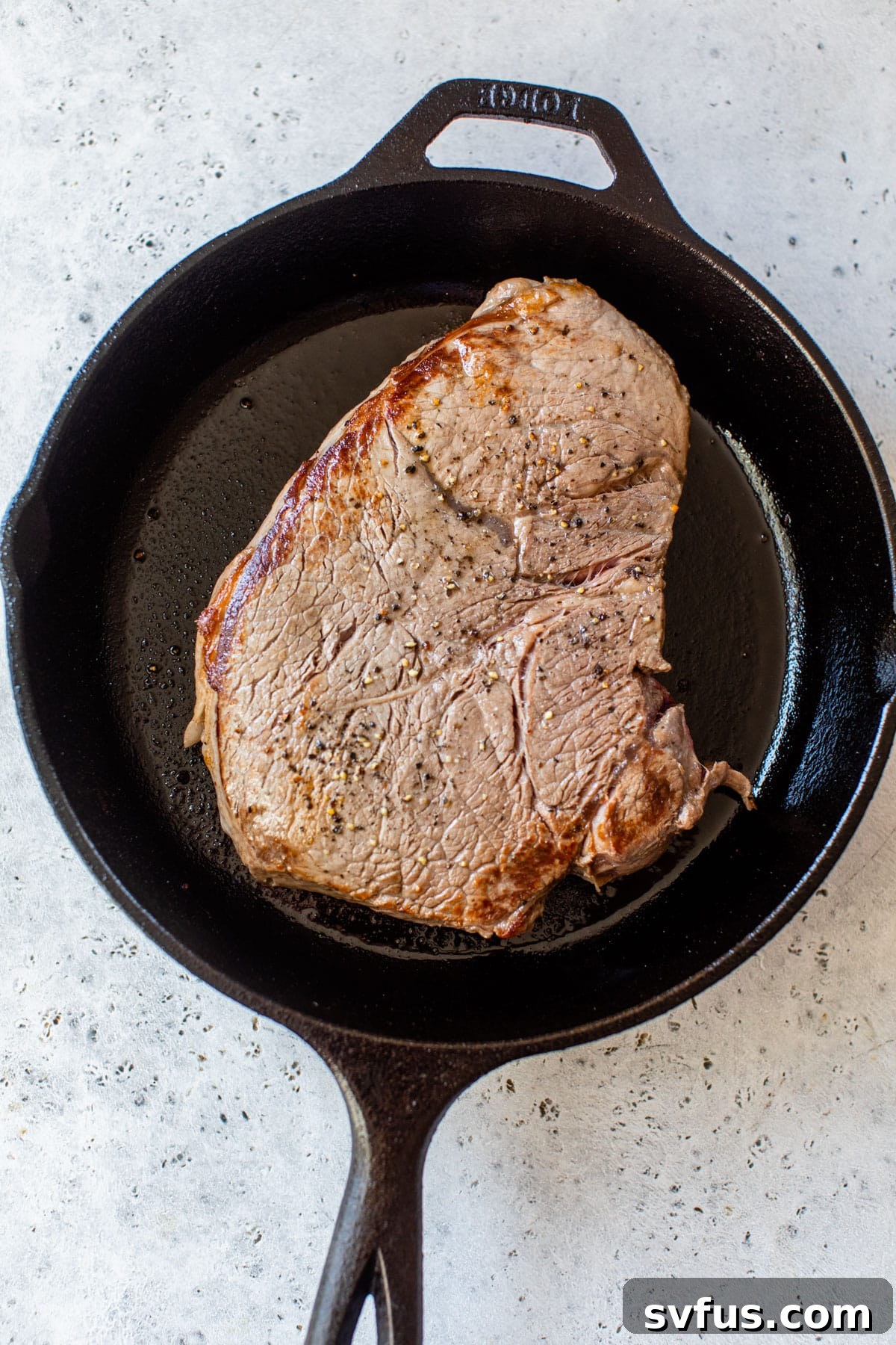 A perfectly seared sirloin steak strip sizzling in a hot cast-iron skillet, forming a delicious brown crust.