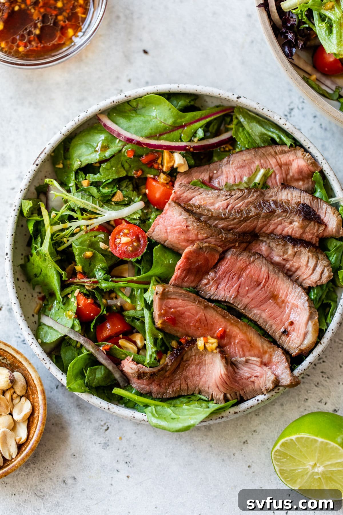 Close-up side view of a beautifully plated Thai Steak Salad in a bowl, showcasing the tender sirloin steak slices, vibrant vegetables, and a generous drizzle of dressing.