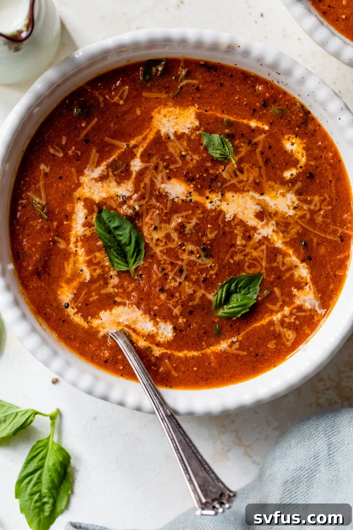 A bowl of creamy tomato basil soup, garnished with a swirl of cream and fresh basil leaves, ready to be enjoyed with a spoon.