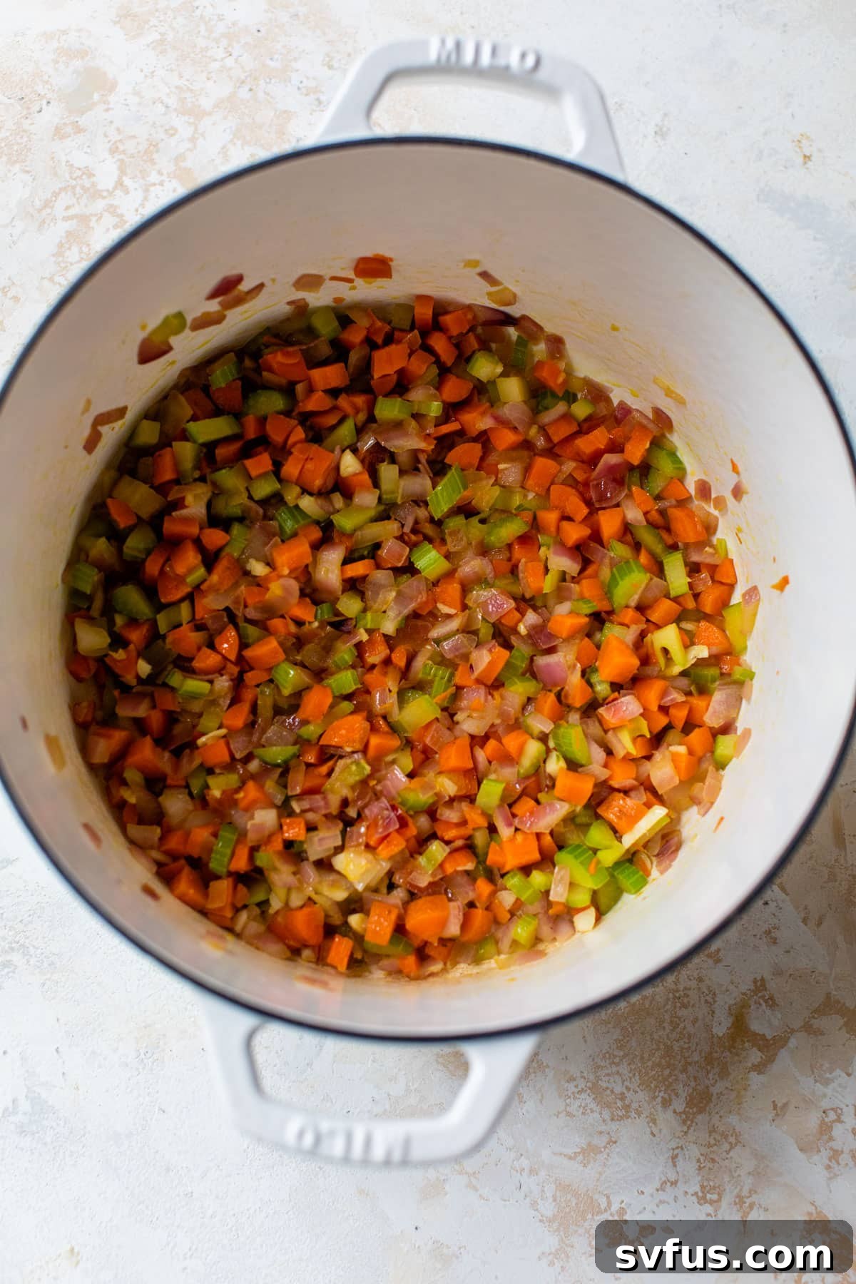 Diced onion, carrots, and celery sautéing in a Dutch oven, building the aromatic base for the soup.