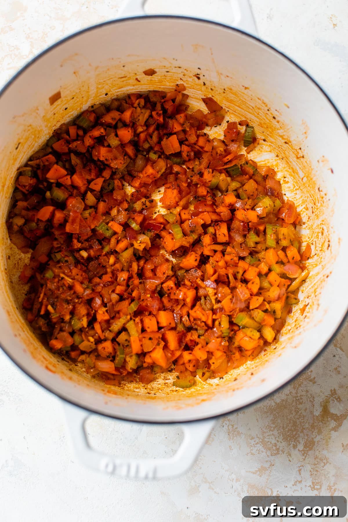 Onion, carrot, and celery sautéing in a Dutch oven with spices and tomato paste being added.