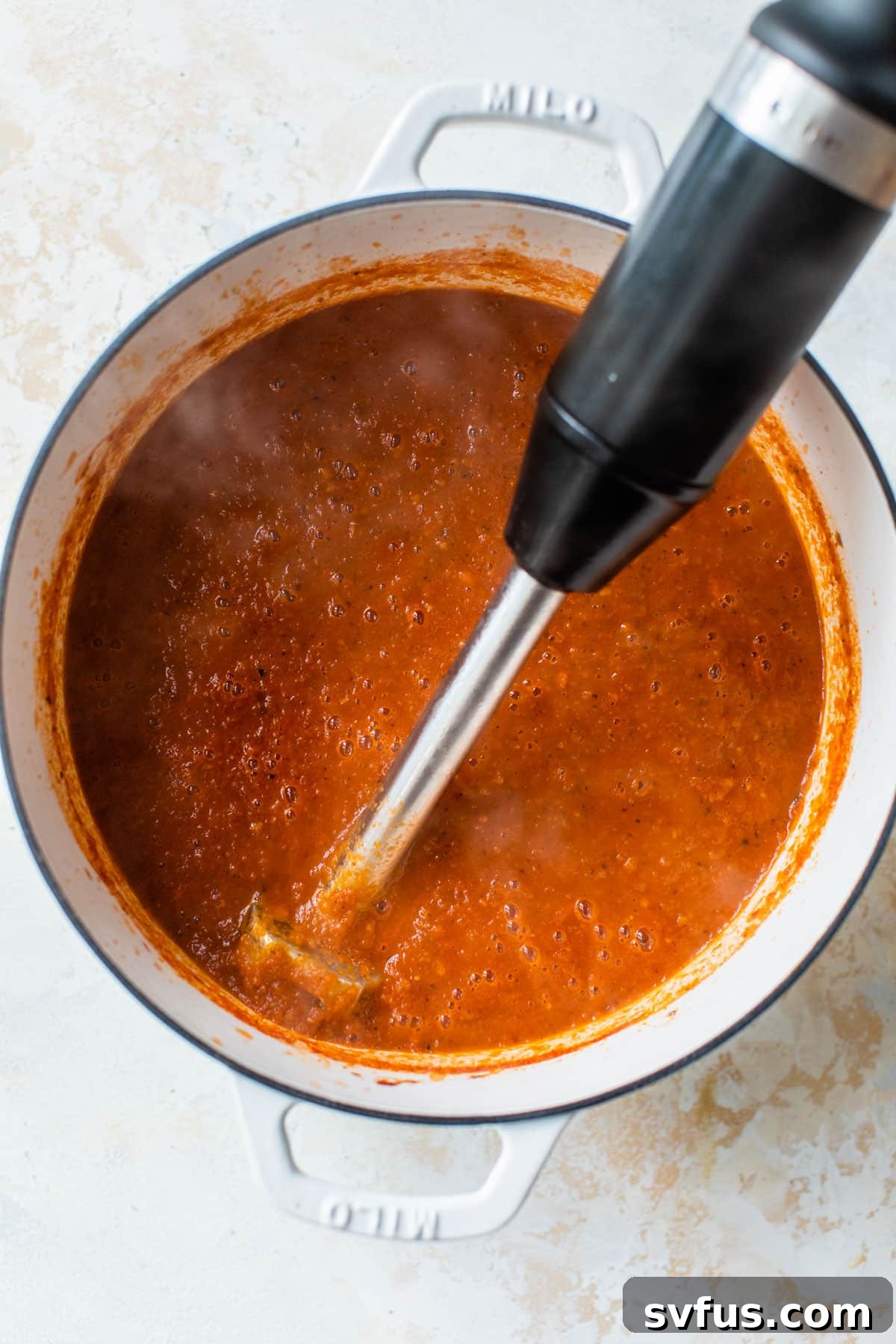 Creamy tomato basil soup being blended to a smooth consistency using an immersion blender directly in a Dutch oven.