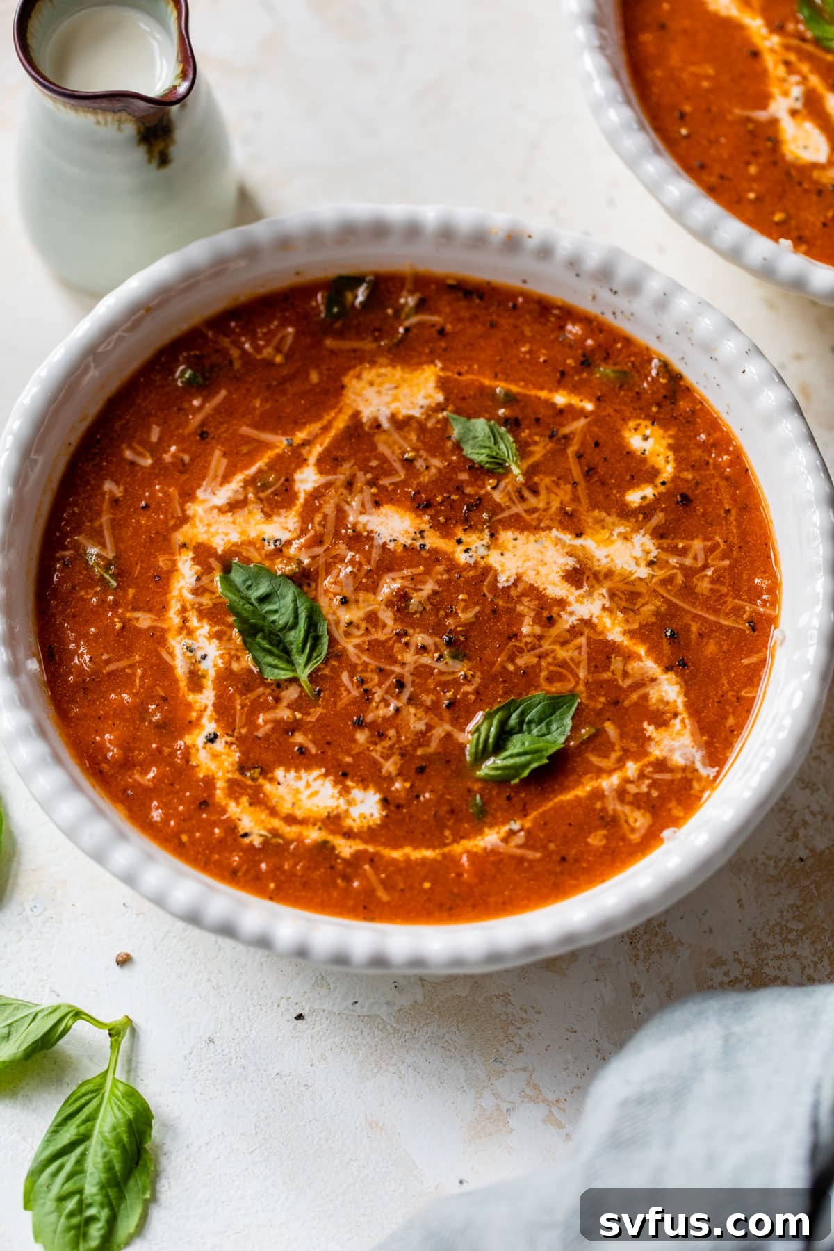 A bowl of creamy tomato basil soup with a drizzle of half & half and fresh basil leaves on top, ready to serve.