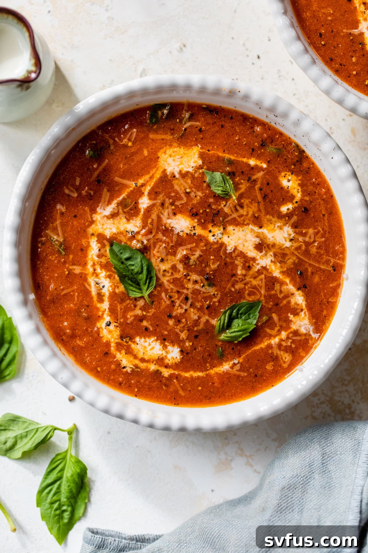 A perfectly portioned bowl of creamy tomato basil soup, garnished with a swirl of cream and fresh basil, ready for a comforting meal.